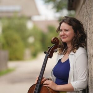 Laura van der Heijden with cello, standing against a wall