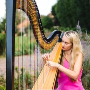 Olivia Jaguers in bright pink dress playing harp outside