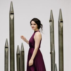 Rachel Mahon standing in concert dress with organ pipes
